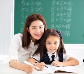 little gile in class writing with teacher helping