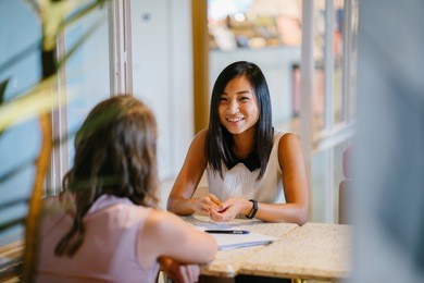 portrait of a young, asian chinese woman in a meeting with a caucasian woman. she is having a meeting or having an interview and is professionally dressed as she has a discussion at a table indoors. 