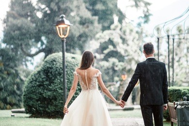 wedding couple kissing in the park under a tree in the rain