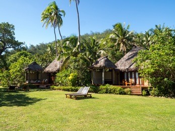 south pacific tropical island bure bungalow deck with day bed looking over garden, oceans and over water bure in fiji