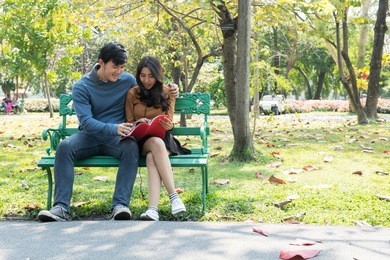 couple in park sitting on a bench. talking to each other in romantic and intimate mood. chinese people.