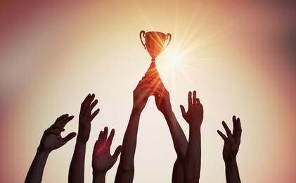 winning team is holding trophy in hands. silhouettes of many hands in sunset.