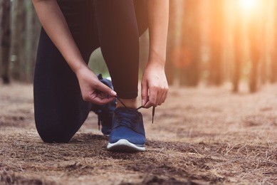 woman tying up shoelaces when jogging in forest background. sneakers rope tying. people and lifestyles concept. healthcare and wellness theme. park and outdoors theme.
