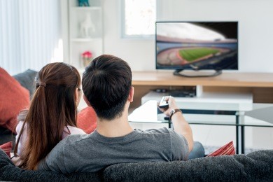 rear view of asian couple watching football at television in living room. football festival concept.