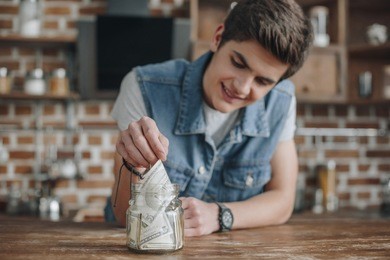 handsome teenager taking dollar banknotes from saving glass jar for money