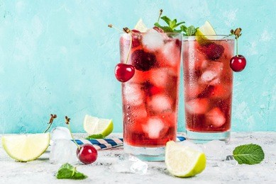 summer iced refreshment drink, cherry cola lemonade or mojito cocktail in tall glass, on light blue and grey background copy space