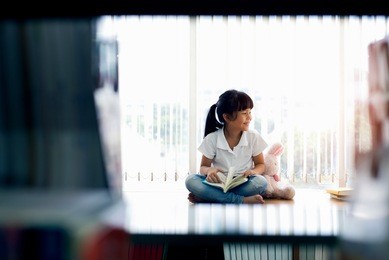 happy cute little child girl reading a book at library 