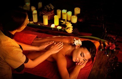 massage of woman in spa salon. girl on candles background treats problem nack and sholders. luxary interior with working hands masseuse. crop of bare back has relax. alternative medicine on very dark