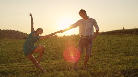 lens flare: lovely barefoot man and woman dance gracefully at stunning summer sunset. cheerful young couple enjoys the soothing spring rain as they have fun dancing on a romantic warm spring evening.