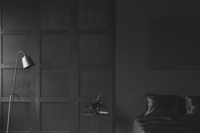 fern on the table between lamp and bed in monochromatic dark bedroom interior with wooden wall