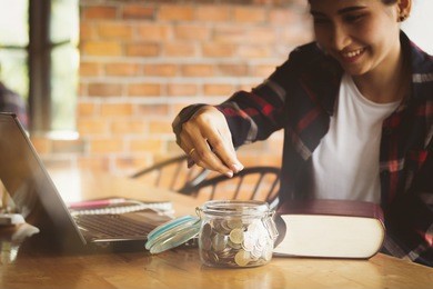 beautiful asia woman,teen,girl putting money coins into the glass bottle for saving money with happy.