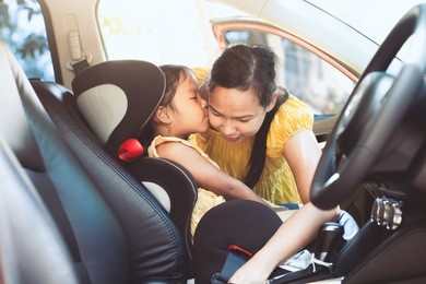asian mother is fastening security belt to her daughter in car seat with care and love