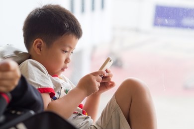 asian chinese boy playing smartphone on bed, watching smartphone, kid use phone and play game, child use mobile, addicted game and cartoon, boy play phone
