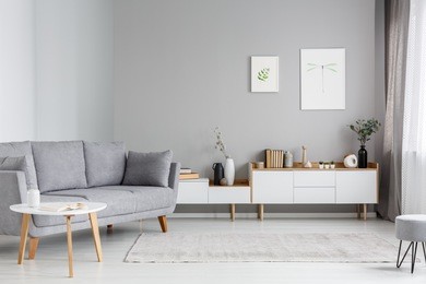 grey settee near white cupboard in minimal living room interior with posters on the wall. real photo