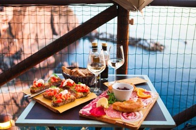 romantic dinner for two at sunset. white wine and tasty italian snack: fresh bruschettes  and meat on the board in outdoor cafe with amazing view in manarola, italy