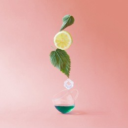 tea cup with fresh nettle leaves, lemon and iceon pink background. minimal fresh natural tea concept.