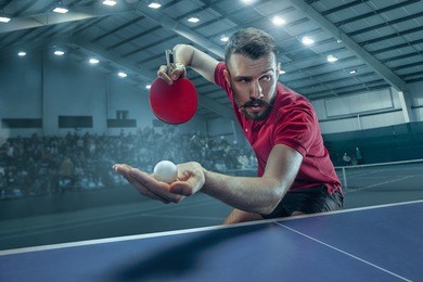 the table tennis player in motion. fit young sports man tennis-player in play on sport arena background with lights. movement, sport game, stobe concepts. professional. human emotions, facial