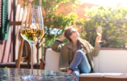 glass of chilled white wine on table over young woman and tuscany backgound