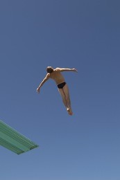 full length of a male diver diving backwards in midair