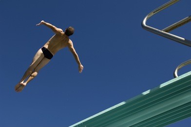 low angle view of a male diver diving from springboard against the blue sky