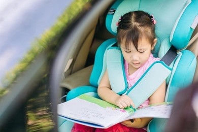kid reading a book wait for mother and sit in the car seat for safety.