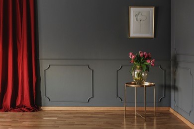 pink tulips on a golden table in the corner of a luxurious interior with molding on dark gray walls and bright red curtains. real photo
