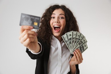 photo of excited happy young business woman with credit card and money isolated over white wall backgound.
