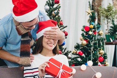 asia lovers couple, boyfriend surprise girlfriendby giving christmas present at sofa with xmas decoration tree at house party,holiday festive celebrating season