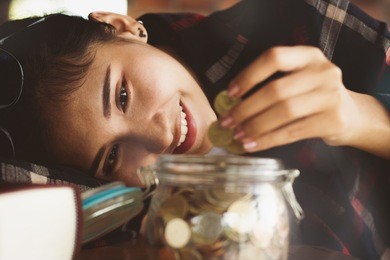 beautiful asia woman ,girl putting money coins into the glass bottle for save money with happy.