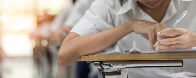 school student's taking educational exam, thinking hard, writing answer with left hand in classroom for education, university admission test  and world literacy day concept