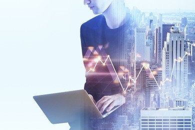 european businessman using laptop computer on light city background with forex chart and copy space. fund management and growth concept. double exposure 