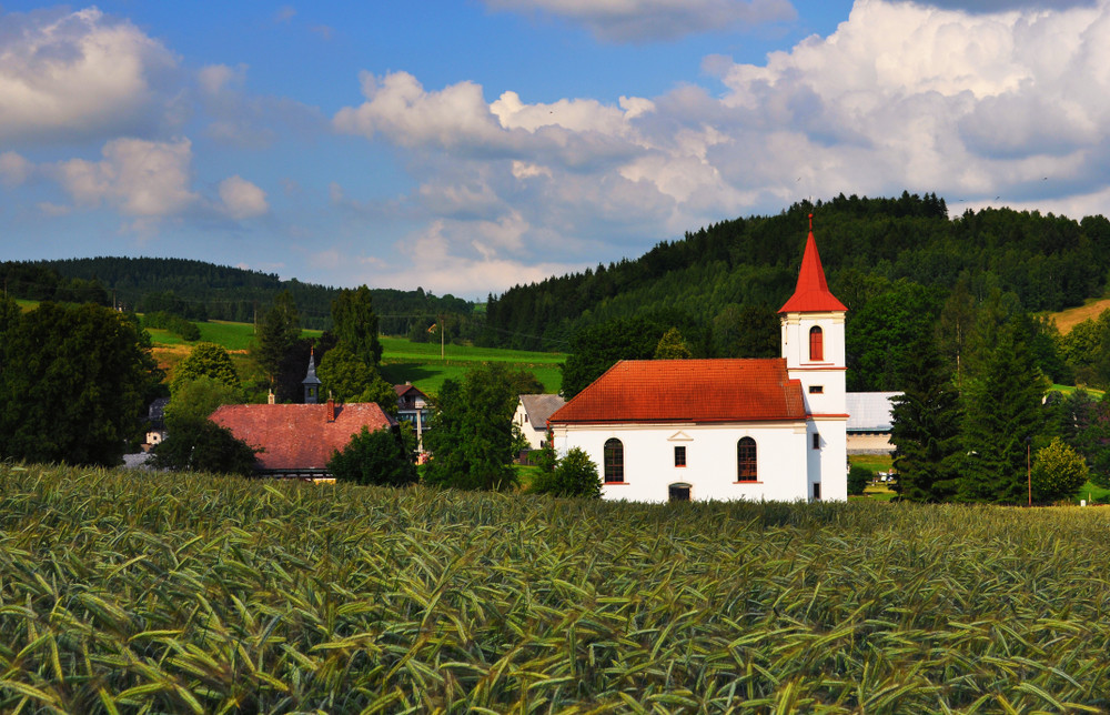 colorful summer bohemian landscape with all features - village with church, field of grain, meadow and woods, blue sky and bright clouds. czech republic