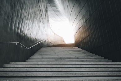 a modern architecture loft concept design of concrete stair with granite surface texture at the walking entrance of a modern exhibition hall building with a sun light at the end of the tunnel.