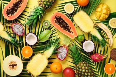 exotic fruits and tropical palm leaves on pastel yellow background - papaya, mango, pineapple, banana, carambola, dragon fruit, kiwi, lemon, orange, melon, coconut, lime. top view
