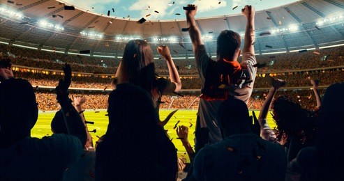 group of cheering fans watch a sport championship on stadium. their team wins and everybody are celebrating this event. people are dressed in casual cloth.