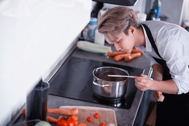 a young asian cook in the kitchen prepares food in a cook suit
