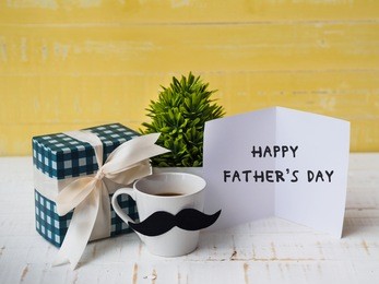 happy father's day concept. gift box, a cup of coffee with mustache and paper card on white and yellow background.