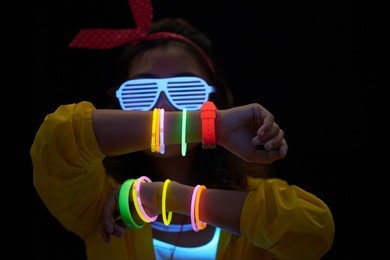 cheerful young woman with neon bracelets in dark room