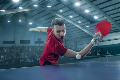 the table tennis player in motion. fit young man in game on sport arena background with lights. movement, sport concepts. professional. human emotions, facial expression