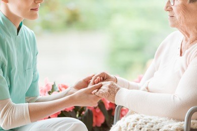 nurse holding hands of disabled elderly woman in a wheelchair