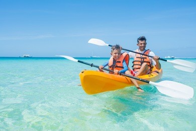 happy cute boy and his father kayaking at tropical sea on yellow kayak