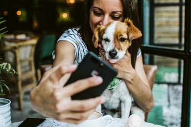 young beautiful woman having great time with her little sweet dog in a restaurant after their meal, taking many pictures. lifestyle and friendship concept.