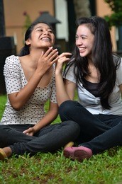two pretty southeast asian girls sharing exciting stories / gossiping  with happy expression at outdoor scene
