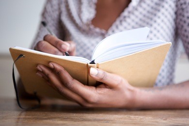 close up partial portrait of black female author at home writing in journal