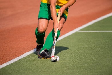 field hockey player, in possesion of the ball, running over an astroturf pitch, looking for a team mate to pass to