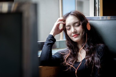 asian woman traveler has listening music with phone and orange headphone inside the train at hua lamphong station at bangkok, thailand.