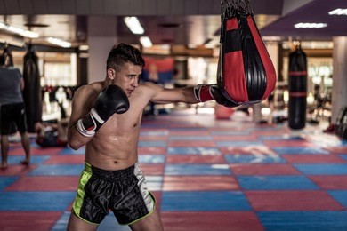young handsome kick boxer training hard and preparing for fight, kicking and punching heavy boxing bag. fighter working out at gym