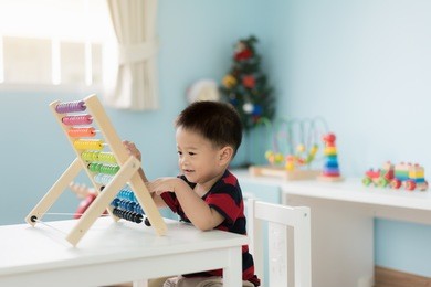 asian toddler baby boy learns to count. cute child playing with abacus toy. little boy having fun indoors at home. educational concept for toddler baby.