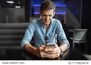 happy young man browsing internet on smartphone while sitting in cafe,