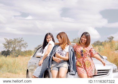 three female tourists stood happily laughing in front of the car with the sky in the background. the concept for travel of female tourists. warm tone. selective focus.